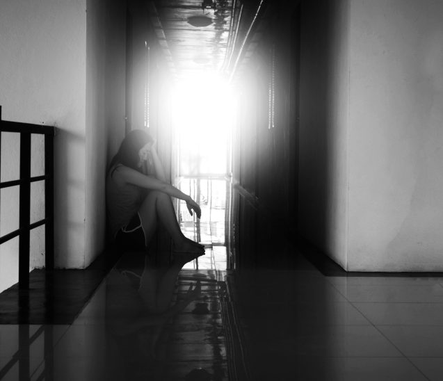 woman in distress sits in empty hallway, head in hands